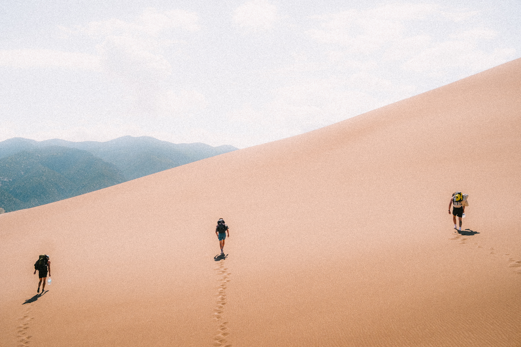 Three hikers climbing a massive sand dune leaving footprints